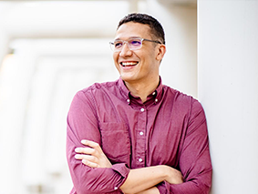 Derek Brekken wearing a red, collared shirt with his arms folded and smiling.