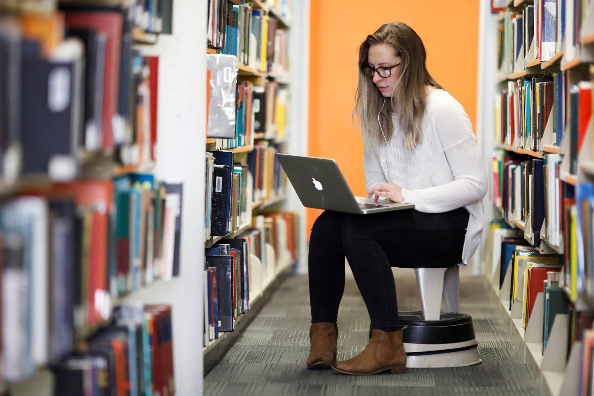 Student sitting in the library working on a laptop computer.